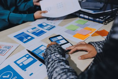 Çalışan bir toplantı sırasında uxui mobil uygulama şablonlarını analiz eden bir grup genç uygulama geliştirici