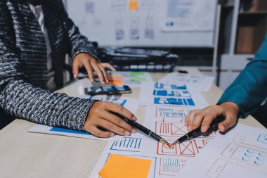 Çalışan bir toplantı sırasında uxui mobil uygulama şablonlarını analiz eden bir grup genç uygulama geliştirici