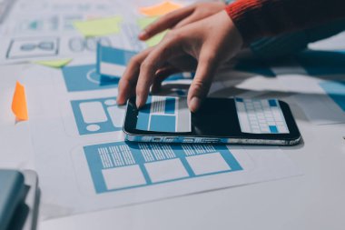 UX UI tasarımcısı prototipi bir telefon üzerinde test ediyor, web sitesi ve mobil uygulama tasarım konseptinde bir web sitesi ve mobil uygulama prototipi için telgraflar üzerinde tartışıyor ve beyin fırtınası yapıyor.