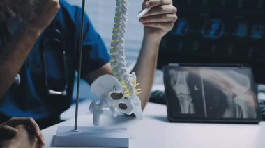 Doktor omurgasını gösteriyor ve hastanın omurga röntgenine durumu açıklıyor.