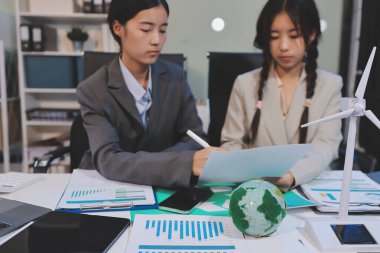 Ekip toplantısında, ESG konu sunumu için dizüstü bilgisayar kullanan Asyalı kadın, çok ırklı iş adamlarından oluşan genç bir gruba liderlik ediyor. Sürdürülebilir iş uygulaması, insanlar ev konseptinde çalışıyor