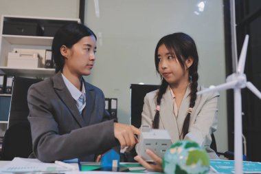 Ekip toplantısında, ESG konu sunumu için dizüstü bilgisayar kullanan Asyalı kadın, çok ırklı iş adamlarından oluşan genç bir gruba liderlik ediyor. Sürdürülebilir iş uygulaması, insanlar ev konseptinde çalışıyor