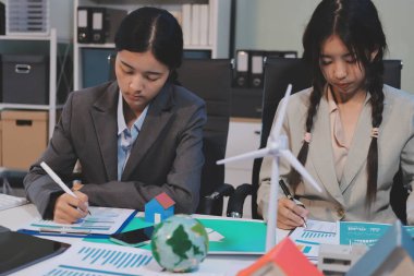 Ekip toplantısında, ESG konu sunumu için dizüstü bilgisayar kullanan Asyalı kadın, çok ırklı iş adamlarından oluşan genç bir gruba liderlik ediyor. Sürdürülebilir iş uygulaması, insanlar ev konseptinde çalışıyor