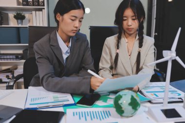 Ekip toplantısında, ESG konu sunumu için dizüstü bilgisayar kullanan Asyalı kadın, çok ırklı iş adamlarından oluşan genç bir gruba liderlik ediyor. Sürdürülebilir iş uygulaması, insanlar ev konseptinde çalışıyor