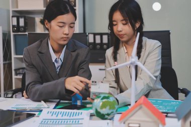 Ekip toplantısında, ESG konu sunumu için dizüstü bilgisayar kullanan Asyalı kadın, çok ırklı iş adamlarından oluşan genç bir gruba liderlik ediyor. Sürdürülebilir iş uygulaması, insanlar ev konseptinde çalışıyor