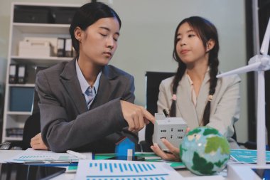 Ekip toplantısında, ESG konu sunumu için dizüstü bilgisayar kullanan Asyalı kadın, çok ırklı iş adamlarından oluşan genç bir gruba liderlik ediyor. Sürdürülebilir iş uygulaması, insanlar ev konseptinde çalışıyor