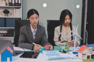 Ekip toplantısında, ESG konu sunumu için dizüstü bilgisayar kullanan Asyalı kadın, çok ırklı iş adamlarından oluşan genç bir gruba liderlik ediyor. Sürdürülebilir iş uygulaması, insanlar ev konseptinde çalışıyor