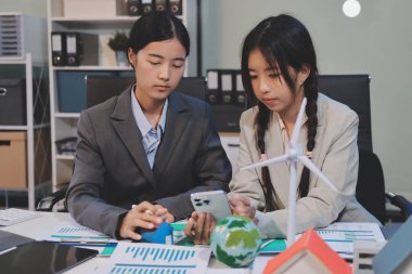 Ekip toplantısında, ESG konu sunumu için dizüstü bilgisayar kullanan Asyalı kadın, çok ırklı iş adamlarından oluşan genç bir gruba liderlik ediyor. Sürdürülebilir iş uygulaması, insanlar ev konseptinde çalışıyor