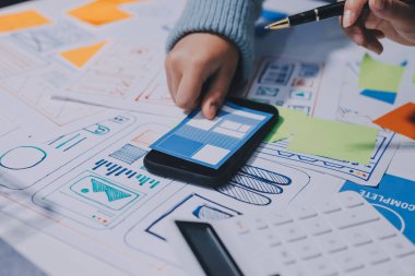 UX UI tasarımcısı prototipi bir telefon üzerinde test ediyor, web sitesi ve mobil uygulama tasarım konseptinde bir web sitesi ve mobil uygulama prototipi için telgraflar üzerinde tartışıyor ve beyin fırtınası yapıyor.