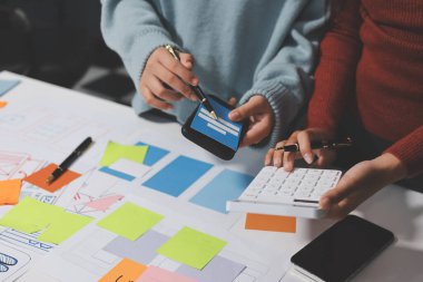 UX UI tasarımcısı prototipi bir telefon üzerinde test ediyor, web sitesi ve mobil uygulama tasarım konseptinde bir web sitesi ve mobil uygulama prototipi için telgraflar üzerinde tartışıyor ve beyin fırtınası yapıyor.