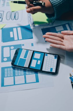 UX UI tasarımcısı prototipi bir telefon üzerinde test ediyor, web sitesi ve mobil uygulama tasarım konseptinde bir web sitesi ve mobil uygulama prototipi için telgraflar üzerinde tartışıyor ve beyin fırtınası yapıyor.
