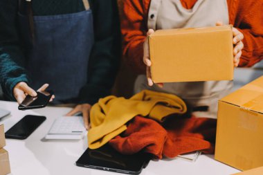 Küçük işletmeler kurma portresi KOBİ sahipleri ve iki Asyalı kadın online siparişleri kontrol ediyor. Ev işlerinde çalışan kutucuklarla çalışan ürünleri satıyorlar.
