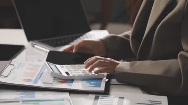İş kadını, ofiste dizüstü bilgisayarla yatırım verilerini ve hesap makinesini analiz ediyor.