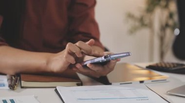 Genç Asyalı işadamı masadaki mali grafiği analiz etmek için hesap makinesi kullanıyor..