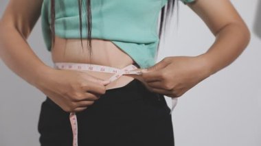 Beyaz arka plan, sağlıklı beslenme ve kilo verme konsepti üzerine ölçüm bandıyla belini ölçen kadın