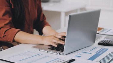 Ofiste dizüstü bilgisayarda çalışan iş kadını, hesap makinesi ve finansal belgeler kullanıyor.