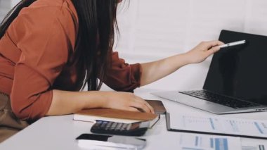 Ofiste bilgisayar, dizüstü bilgisayar, defter ve hesap makinesiyle çalışan genç bir kadın.