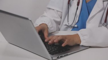 Genç doktor ofiste dizüstü bilgisayarla çalışıyor.