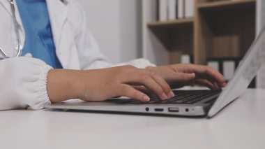 Doktor, hastanedeki ya da klinikteki masada otururken dizüstü bilgisayar kullanıyor. Doktor ve hasta tıbbi hizmet üzerinde çalışıyor. Sağlık ve Tıp Konsepti