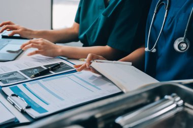 Two doctors and a female nurse meet at a table in the hospital, collaborating on medical tasks using laptops and computers