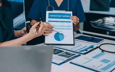Two doctors and a female nurse meet at a table in the hospital, collaborating on medical tasks using laptops and computers