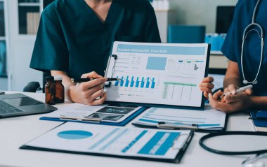 Two doctors and a female nurse meet at a table in the hospital, collaborating on medical tasks using laptops and computers