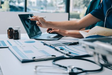 Two doctors and a female nurse meet at a table in the hospital, collaborating on medical tasks using laptops and computers