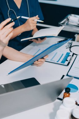 Two doctors and a female nurse meet at a table in the hospital, collaborating on medical tasks using laptops and computers