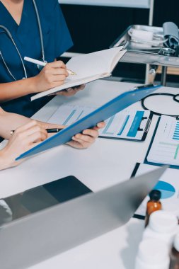 Two doctors and a female nurse meet at a table in the hospital, collaborating on medical tasks using laptops and computers