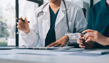 Medical team meeting analyzing blood test results in hospital laboratory. Doctors and scientists in lab coats are having a discussion about blood test result, holding test tubes and taking notes.