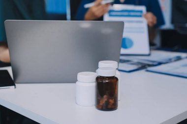 Two doctors and a female nurse meet at a table in the hospital, collaborating on medical tasks using laptops and computers