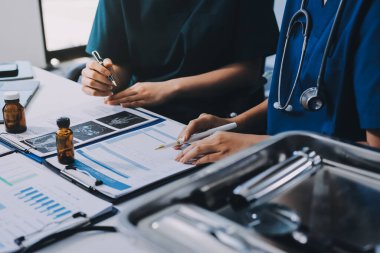 Two doctors and a female nurse meet at a table in the hospital, collaborating on medical tasks using laptops and computers