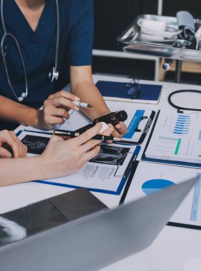 Two doctors and a female nurse meet at a table in the hospital, collaborating on medical tasks using laptops and computers