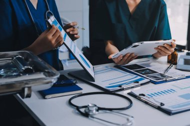 Two doctors and a female nurse meet at a table in the hospital, collaborating on medical tasks using laptops and computers