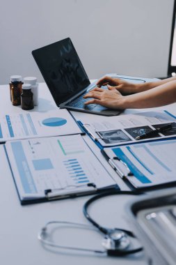 Two doctors and a female nurse meet at a table in the hospital, collaborating on medical tasks using laptops and computers