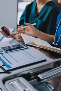 Two doctors and a female nurse meet at a table in the hospital, collaborating on medical tasks using laptops and computers