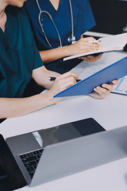 Two doctors and a female nurse meet at a table in the hospital, collaborating on medical tasks using laptops and computers