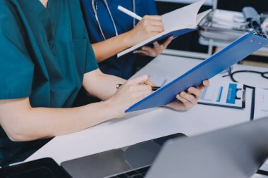 Two doctors and a female nurse meet at a table in the hospital, collaborating on medical tasks using laptops and computers