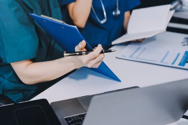 Two doctors and a female nurse meet at a table in the hospital, collaborating on medical tasks using laptops and computers