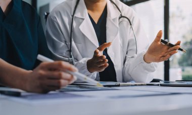 Medical team meeting analyzing blood test results in hospital laboratory. Doctors and scientists in lab coats are having a discussion about blood test result, holding test tubes and taking notes.