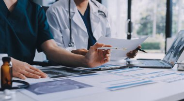 Medical team meeting analyzing blood test results in hospital laboratory. Doctors and scientists in lab coats are having a discussion about blood test result, holding test tubes and taking notes.