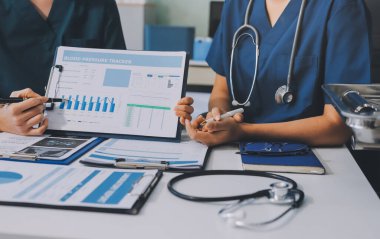 Two doctors and a female nurse meet at a table in the hospital, collaborating on medical tasks using laptops and computers