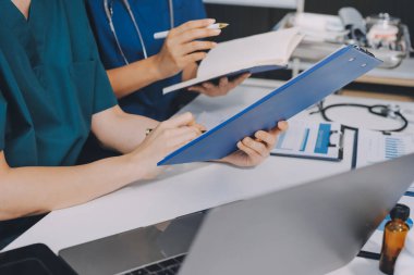 Two doctors and a female nurse meet at a table in the hospital, collaborating on medical tasks using laptops and computers