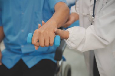 Yaşlı Asyalı adam hemşirenin desteğiyle fizyoterapiste gidiyor. Oturma odasındaki kanepede oturan yaşlı erkek hasta bakıcısı için halterli egzersiz yapıyor..