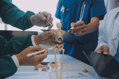 Çok ırklı tıbbi ekip, beyaz laboratuvar önlüklü ve ameliyat önlüklü doktorlarla toplantı yapıyor. Hasta kayıtlarını tartışıyorlar.