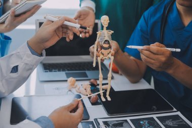 Çok ırklı tıbbi ekip, beyaz laboratuvar önlüklü ve ameliyat önlüklü doktorlarla toplantı yapıyor. Hasta kayıtlarını tartışıyorlar.