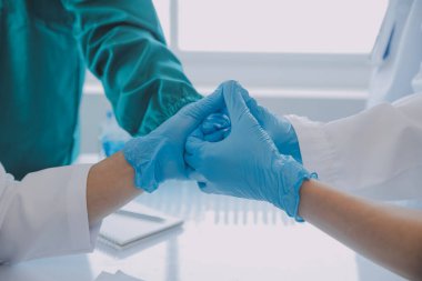 Çok ırklı tıbbi ekip, beyaz laboratuvar önlüklü ve ameliyat önlüklü doktorlarla toplantı yapıyor. Hasta kayıtlarını tartışıyorlar.