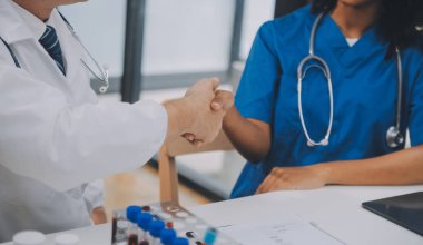 Doktor ve hasta ofiste el sıkışıyorlar. Masada oturuyorlar, eller kapalı.