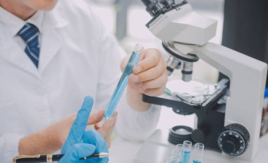 Biyoteknoloji laboratuvarında çalışan bilim adamı veya laboratuvar önlüğü, araştırma için mikroskop ekipmanı ve klinik laboratuarında cam şişede karıştırıcı reaktörler..