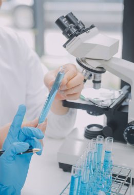 Biyoteknoloji laboratuvarında çalışan bilim adamı veya laboratuvar önlüğü, araştırma için mikroskop ekipmanı ve klinik laboratuarında cam şişede karıştırıcı reaktörler..